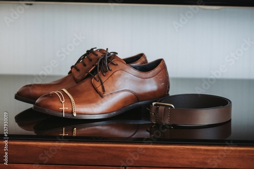 Closeup of brown formal oxford shoes and a leather belt placed on a wooden surface photo