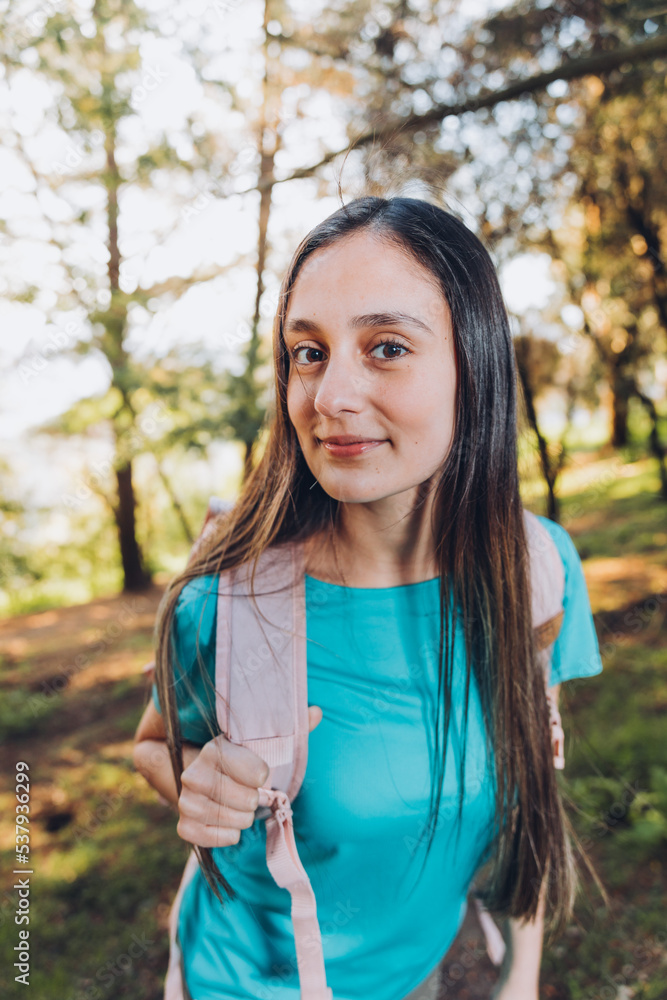 Self-confidence. Teenage girl looking at camera carrying backpack with serene smile in forest. Self-confidence. Teenage girl looking at camera carrying backpack with serene smile in forest.