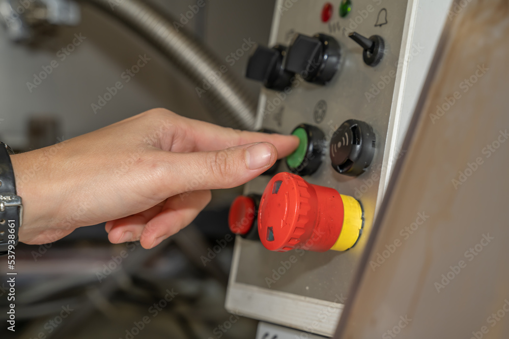 Bouton de gestion d'une machine industrielle en usine actionné par la main d'un femme Bouton de gestion d'une machine industrielle en usine actionné par la main d'un femme