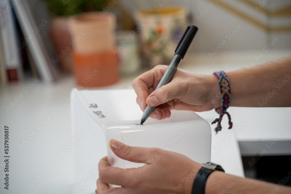 Ecriture avec un feutre sur une boite en plastique par une main de femme Ecriture avec un feutre sur une boite en plastique par une main de femme