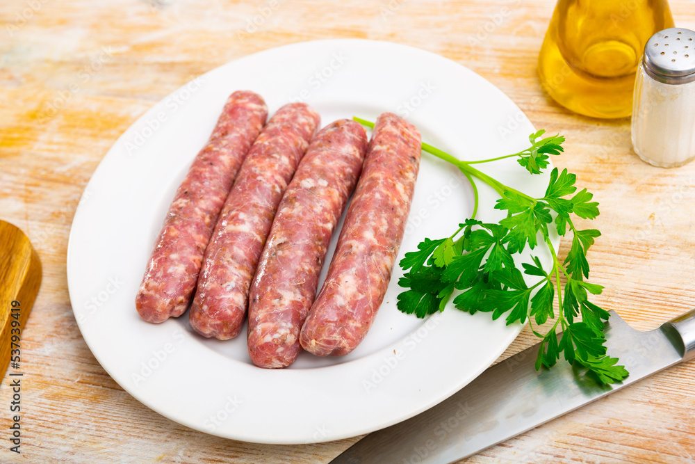 Plate with raw popular Catalan sausages botifarra and fresh greens prepared for cooking on table with knife. Traditional meat products