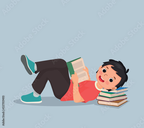 Cute little boy reading book lying on the floor with head on stack of books 