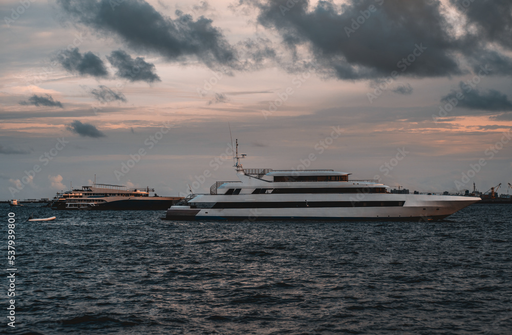 Low-key view of two recreational vessels in the waters of Male island of Maldives with an evening skyscape in the background; big multideck safari boats in the ocean on a sunset with a dramatic sky