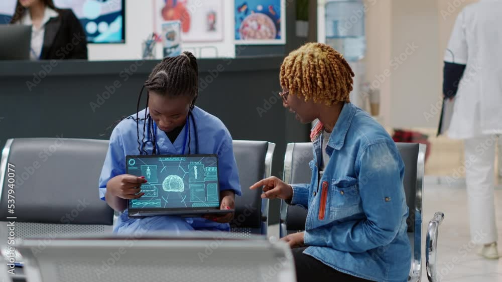 African american patient analyzing brain neurology scan at medical consultation in reception lobby with nurse. Woman and assistant looking at tomography and neural system diagnosis on laptop. African american patient analyzing brain neurology scan at medical consultation in reception lobby with nurse. Woman and assistant looking at tomography and neural system diagnosis on laptop.