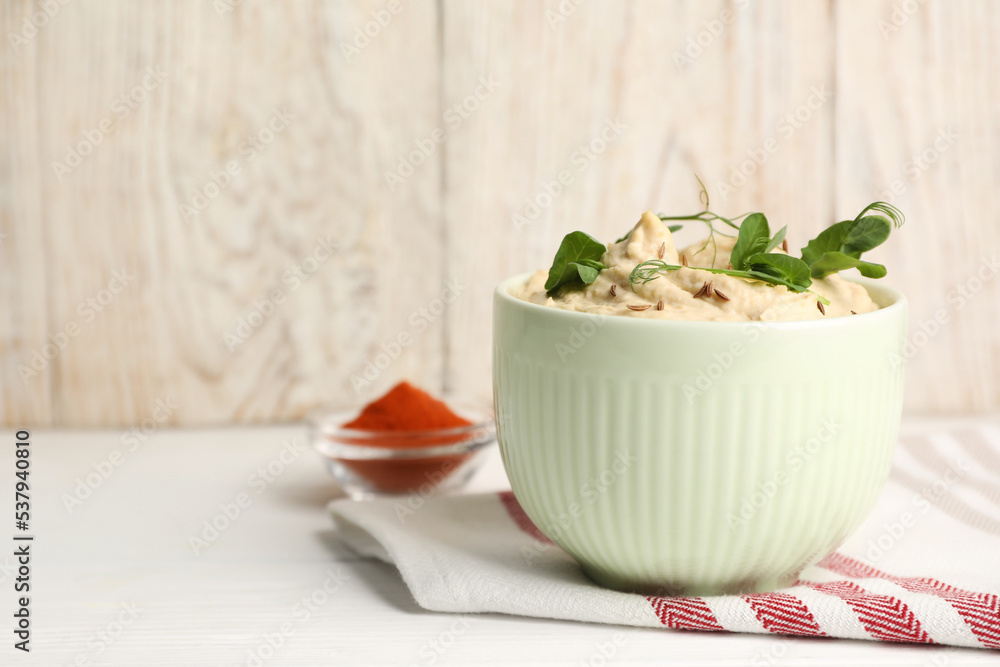 Bowl of tasty hummus with pea leaves on white wooden table, space for text Bowl of tasty hummus with pea leaves on white wooden table, space for text