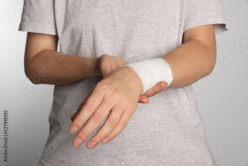 Woman with wrist wrapped in medical bandage on light grey background, closeup © New Africa