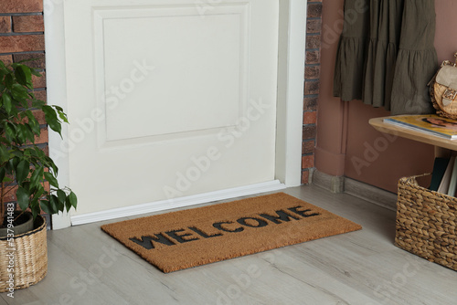 Door mat with word Welcome on wooden floor in hall