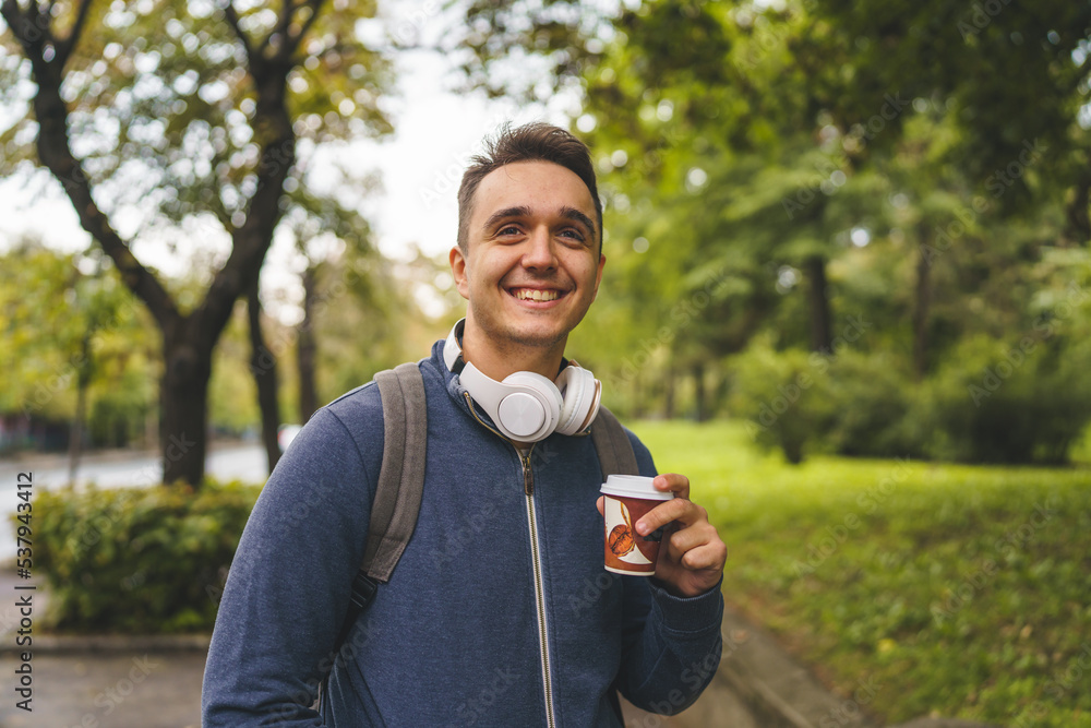 One young adult caucasian man walking in the city or town near park with cup of coffee in autumn or spring day happy male tourist standing alone real people copy space One young adult caucasian man walking in the city or town near park with cup of coffee in autumn or spring day happy male tourist standing alone real people copy space