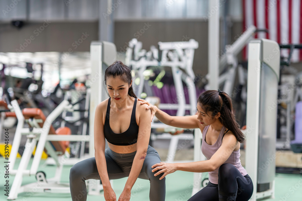 Female fitness instructor showing exercise progress to a young athletic woman at the gym and smiling cheerfully while exercising with his fitness coach and training.