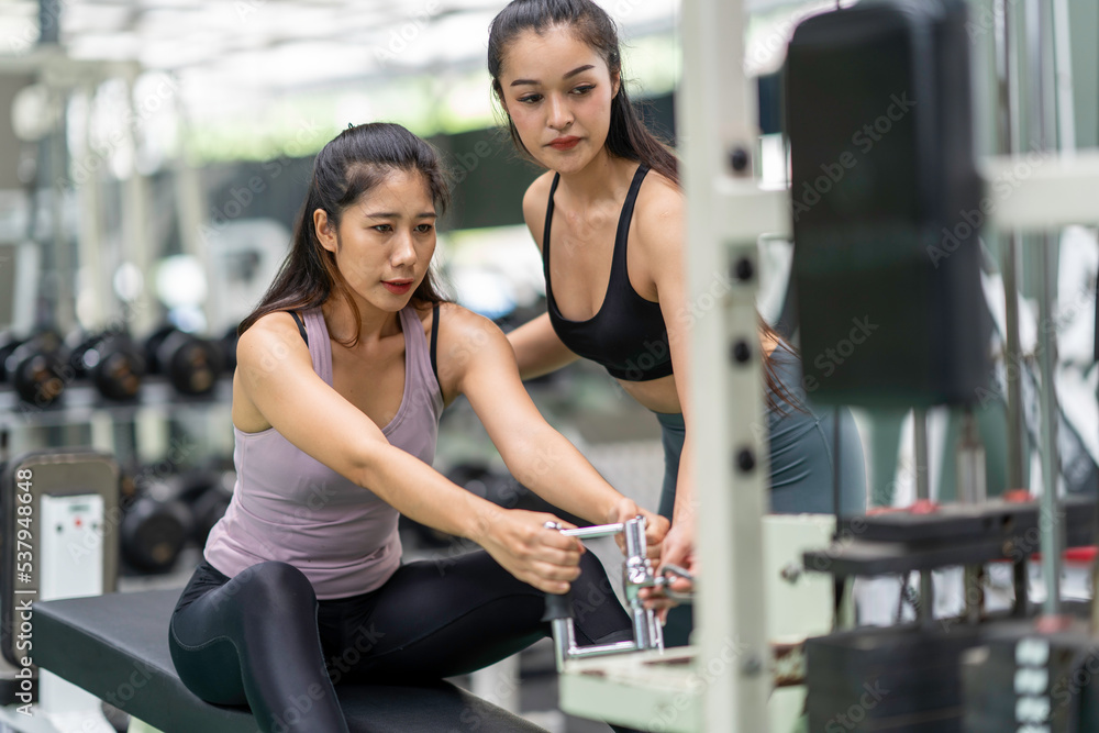 Female trainer teaches Asian women fitness pulling cable the way they exercise in the gym. Female trainer teaches Asian women fitness pulling cable the way they exercise in the gym.