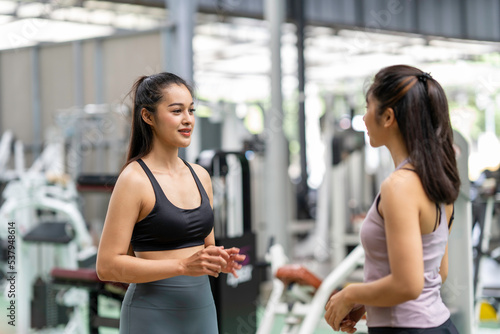 Female fitness instructor showing exercise progress to a young athletic woman at the gym and smiling cheerfully while exercising with his fitness coach and training.