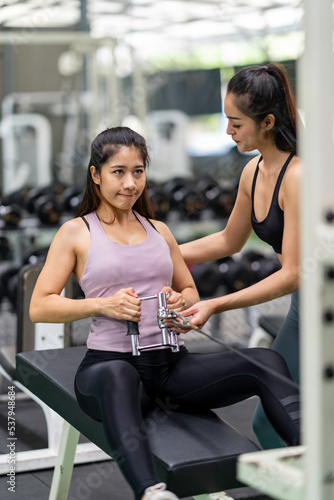 Female trainer teaches Asian women fitness pulling cable the way they exercise in the gym.
