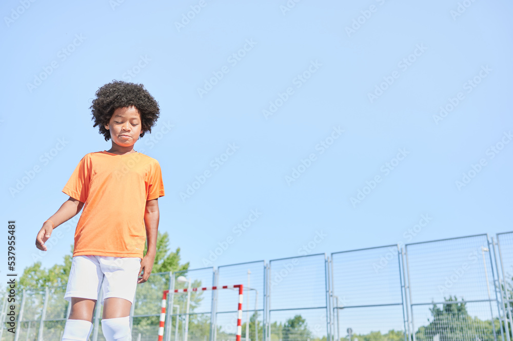 Smiling young boy with afro hair wears the orange Netherlands national football team equipment while warms up to play football in a training field. Smiling young boy with afro hair wears the orange Netherlands national football team equipment while warms up to play football in a training field.