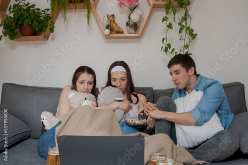 Three young friends, watching a movie on the laptop on the laptop, scared.