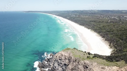 Drone aerial pan down to beautiful blue beach with waves and white sand near cliff side photo