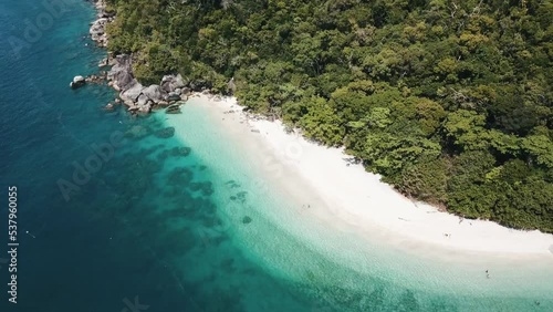 Drone aerial with slow pan up over tropical clear blue with white sandy beach and tropical forest photo