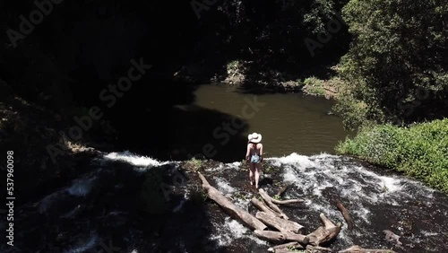 Drone aerial in nature with a woman walking on the ledge of a waterfall exploring with the camera panning down photo