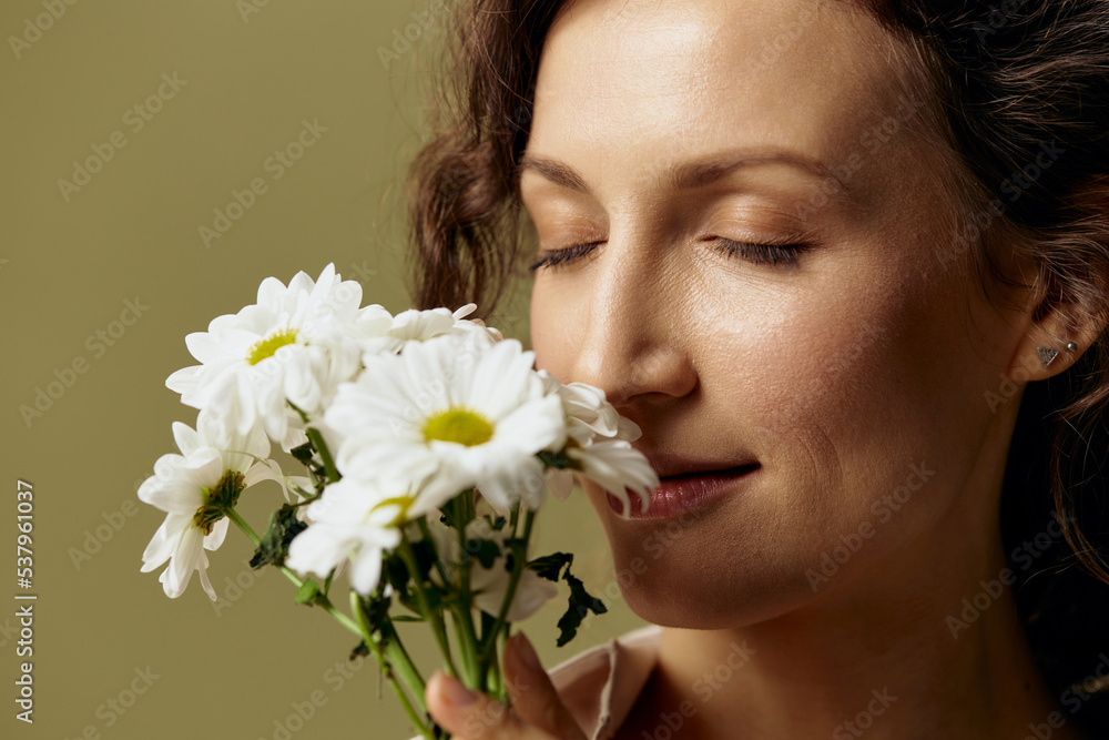 Close up portrait of cheerful curly female in linen casual shirt hold chamomiles enjoy flowers smell close eyes posing isolated on olive green pastel background. Nature is beauty concept. Copy space Close up portrait of cheerful curly female in linen casual shirt hold chamomiles enjoy flowers smell close eyes posing isolated on olive green pastel background. Nature is beauty concept. Copy space