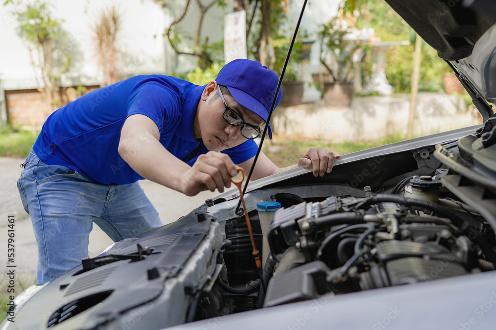 A young man checks the oil level of the car and fixes the tire pressure gauge before leaving.