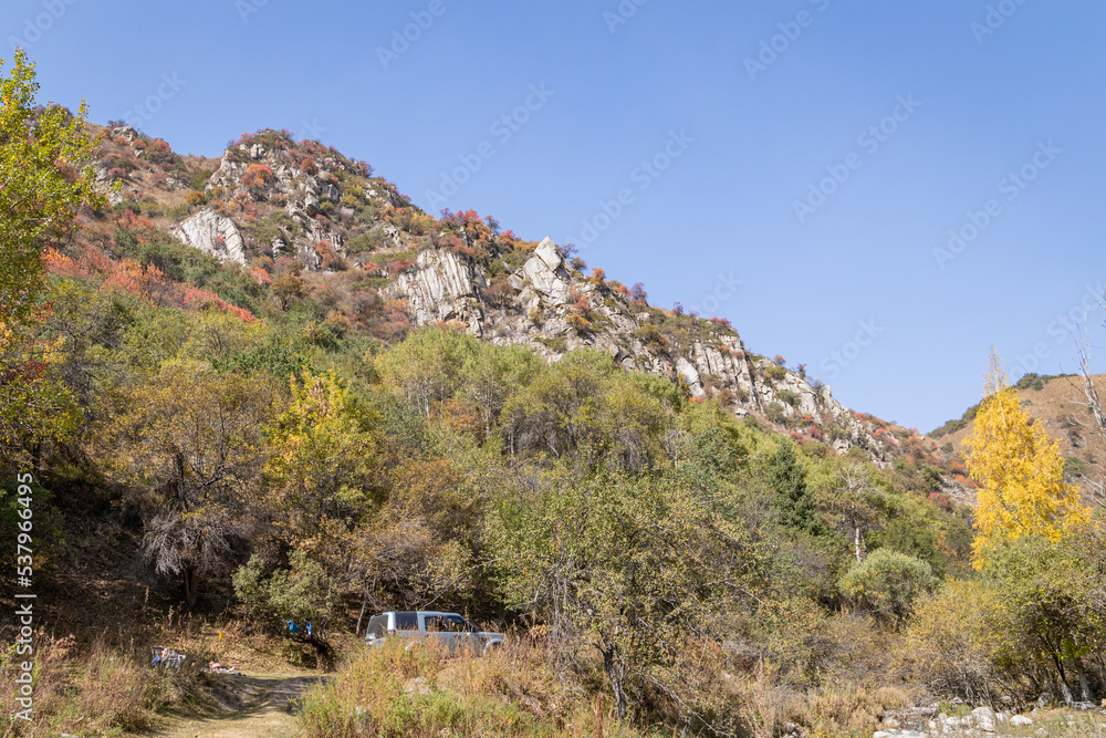 Autumn landscape - blue sky, yellow ground, mountains and hills, green and yellow foliage of the forest trees