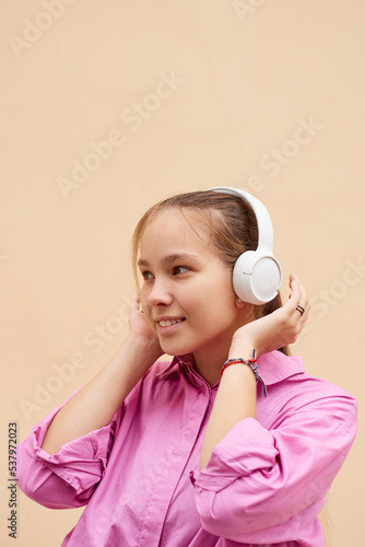 Smiling teenager schoolgirl in pink shirt listening to music using wireless headphones