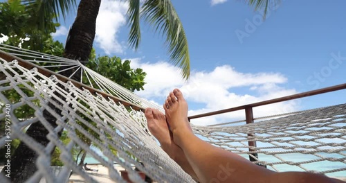 Luxury travel vacation concept video - closeup of feet of relaxing woman sleeping on hammock at luxury resort in the tropical sun on luxury travel vacation.
