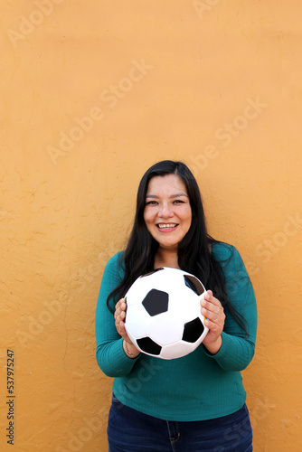 Latino adult woman plays with a soccer ball very excited that she is going to see the World Cup and wants to see her team win © Arlette