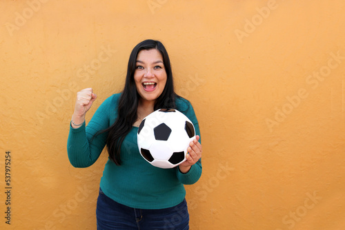 Latino adult woman plays with a soccer ball very excited that she is going to see the World Cup and wants to see her team win © Arlette