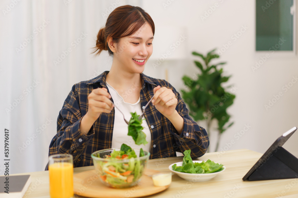 Lifestyle in living room concept, Young Asian woman looking at tablet and eating vegetable salad
