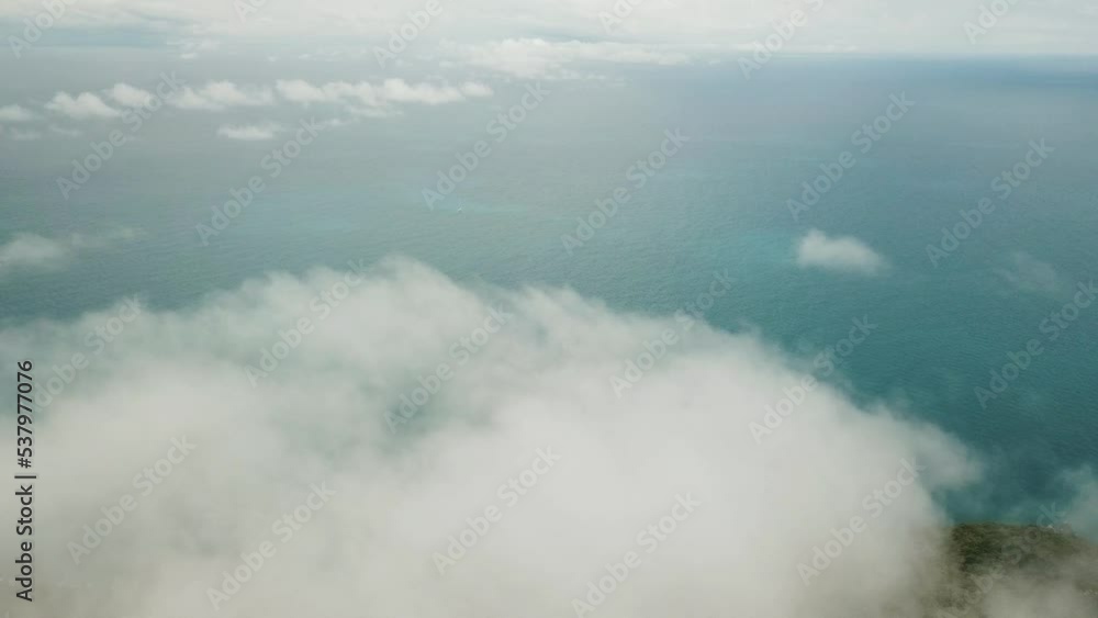 Drone aerial above clouds panning down to tropical island with blue water in summer Drone aerial above clouds panning down to tropical island with blue water in summer