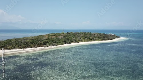 Drone aerial moving towards island that's tropical with white sandy beach and blue reef water photo