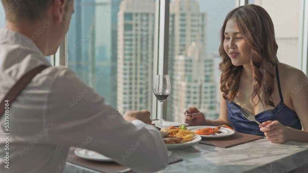 Young beautiful elegant asian female lady having a good time with her caucasian boyfriend eating lunch drinking red wine in a rooftop restaurant and lounge with nice view of the Bangkok city skyline Young beautiful elegant asian female lady having a good time with her caucasian boyfriend eating lunch drinking red wine in a rooftop restaurant and lounge with nice view of the Bangkok city skyline