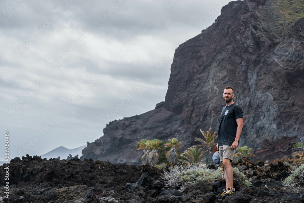 Caucasian young man standing in the black rocks in a cloudy day