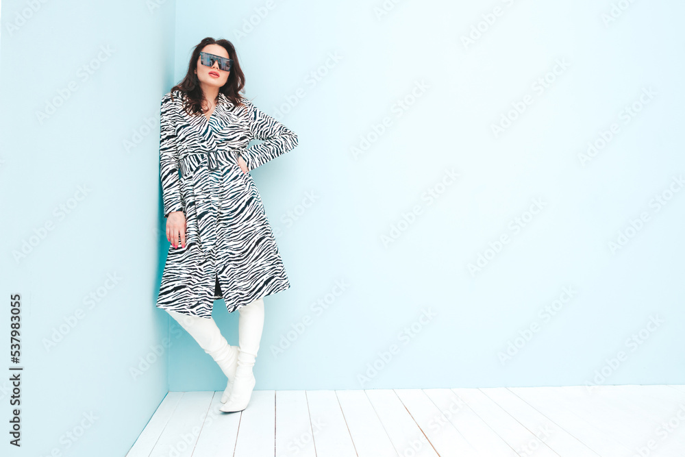High fashion portrait of young beautiful brunette woman wearing nice trendy summer zebra coat. Sexy fashion model posing near light blue wall in studio. Fashionable female indoors in sunglasses High fashion portrait of young beautiful brunette woman wearing nice trendy summer zebra coat. Sexy fashion model posing near light blue wall in studio. Fashionable female indoors in sunglasses