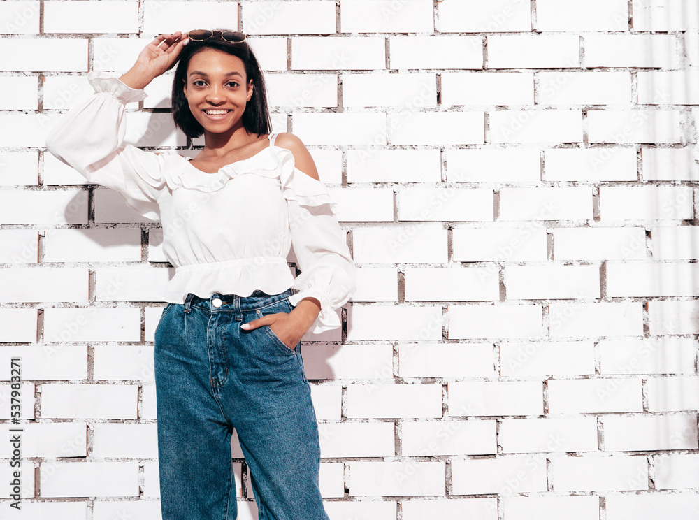 Portrait of young beautiful woman. Smiling model dressed in summer jeans clothes. carefree female posing near white brick wall in studio. Tanned and cheerful Portrait of young beautiful woman. Smiling model dressed in summer jeans clothes. carefree female posing near white brick wall in studio. Tanned and cheerful