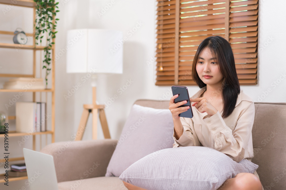 Concept of relaxation at home, Young Asian woman use smartphone to chatting with friends on sofa Concept of relaxation at home, Young Asian woman use smartphone to chatting with friends on sofa