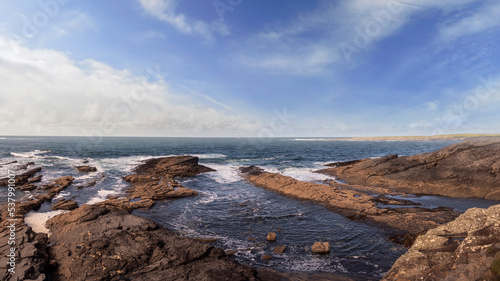 Rough stone coast line and powerful waves in the ocean. Spanish point part of Wild Atlantic Way tourist route, county Clare, Ireland. Warm sunny day, blue cloudy sky and water. Irish seascape.