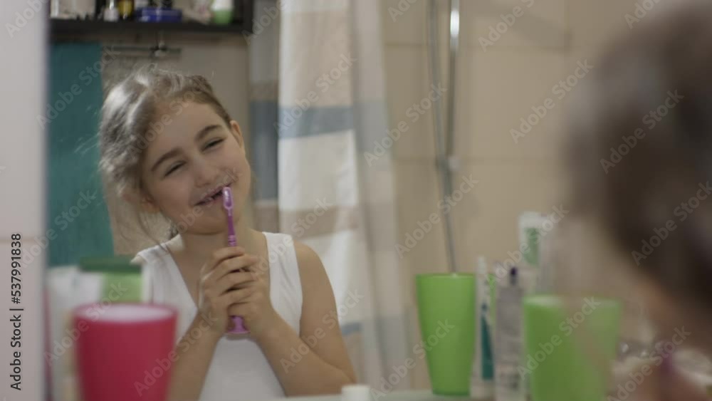 Close-up Portrait Young Little Girl Dancing Singing With Toothbrush in Bathroom Looking at Mirror Reflection. Daily Routine Dental Hygiene. Happy Portrait Caucasian Toothless Child Dancing in Bathroom Close-up Portrait Young Little Girl Dancing Singing With Toothbrush in Bathroom Looking at Mirror Reflection. Daily Routine Dental Hygiene. Happy Portrait Caucasian Toothless Child Dancing in Bathroom