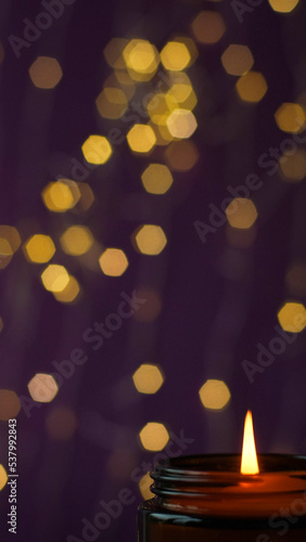 Close-up burning candle in a brown glass with selective focus on golden bokeh background