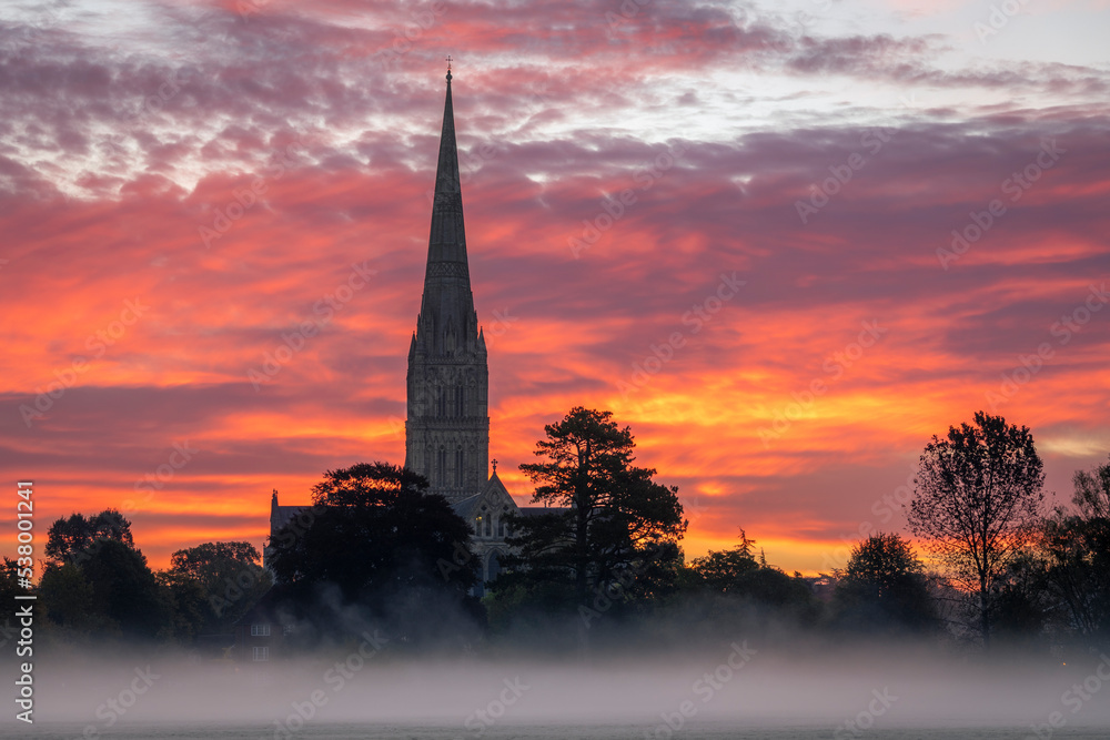 Obraz premium October misty morning sunrise behind Salisbury Cathedral from the Harnham water meadows Wilitshire south west England