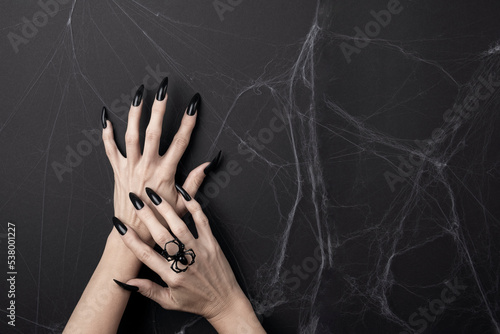 Hands with long black nails and spider ring on a black background with cobwebs. Happy Halloween holiday concept