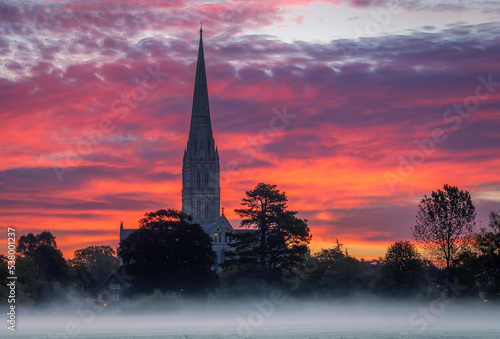 October misty morning sunrise behind Salisbury Cathedral from the Harnham water meadows Wilitshire south west England photo