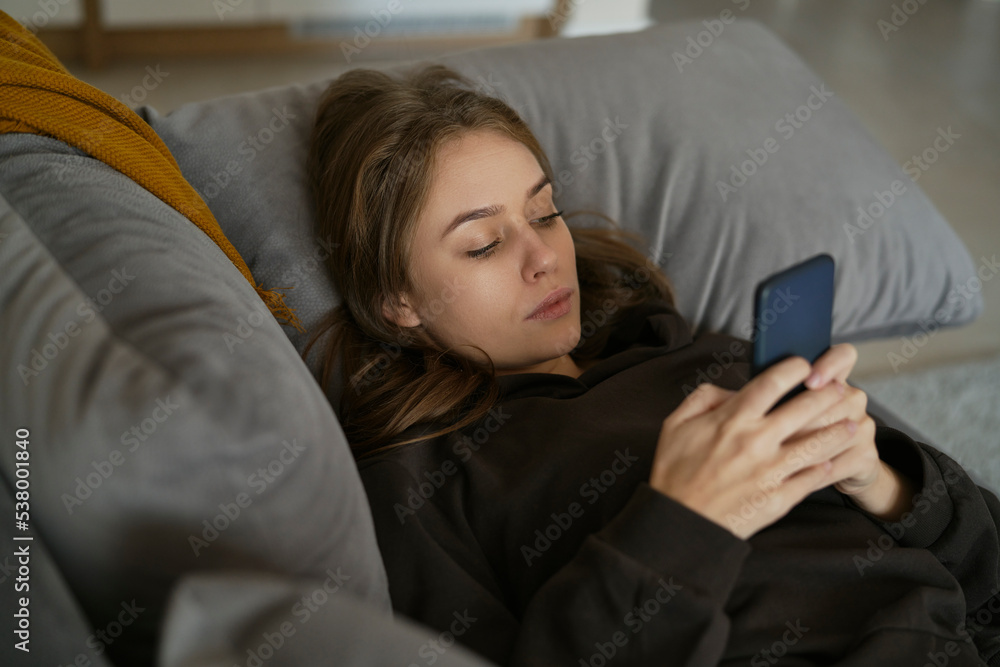 Caucasian woman lying down on the couch and using mobile phone Caucasian woman lying down on the couch and using mobile phone