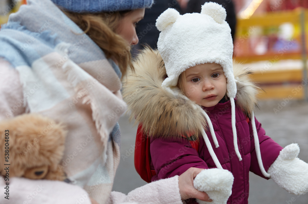 Fototapeta premium Mother and daughter are walking around the city on Christmas and New Year holidays. Parent and little child having fun outdoors