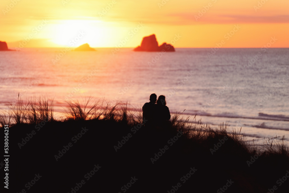 couple sitting backlit watching the sea at sunset