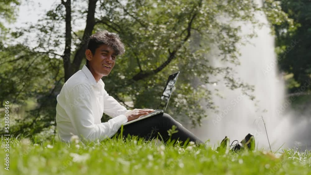 Enthusiastic young man working remotely with laptop at park, sunny day Enthusiastic young man working remotely with laptop at park, sunny day