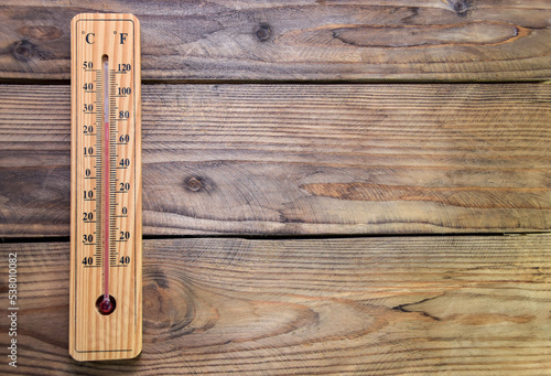 On a wooden wall hangs a wooden mercury thermometer at around 25 with a scale from minus 40 to plus 50 degrees near zero. Air temperature in the room. 25 degrees Celsius or 80 degrees Fahrenheit.