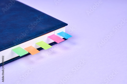 An office notepad with colorful sticky page markers sandwiched between pages on purple background © marketlan