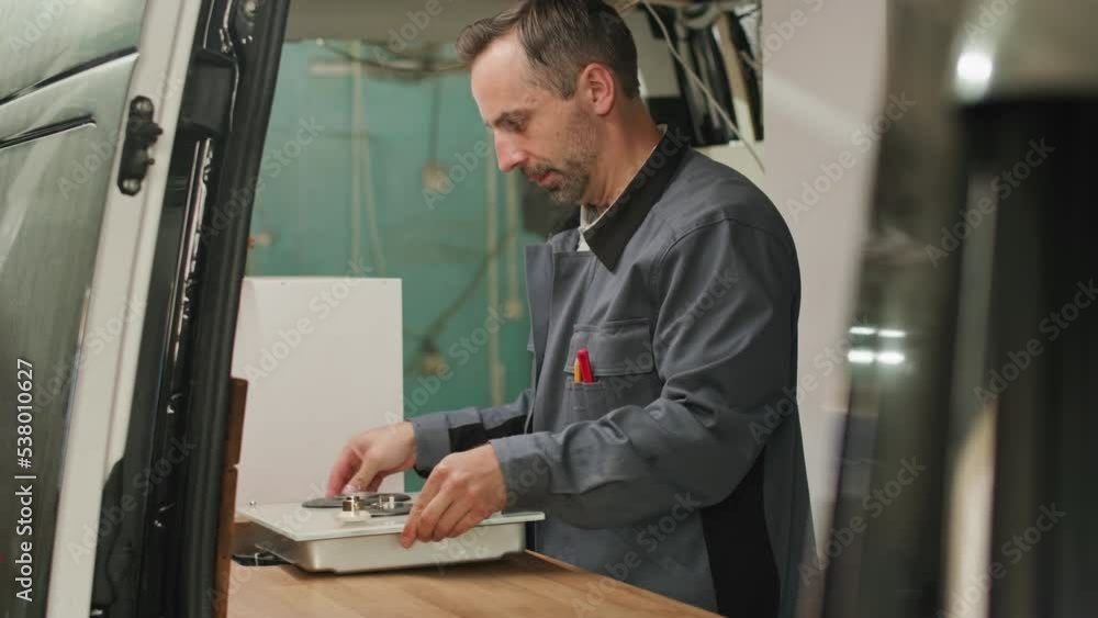 Middle aged Caucasian man bringing cooker while assembling kitchen in camper van Middle aged Caucasian man bringing cooker while assembling kitchen in camper van