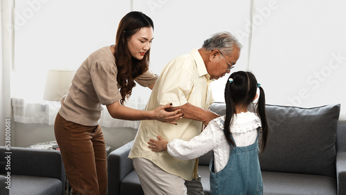 Asian family, Daughter and granddaughter take care support senior mature grandfather who is suffering from knee pain walking outside to take a walk And grandpa with a stick, elderly health care.